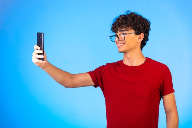 Hombre de camisa roja tomando selfie o haciendo una llamada telefónica y divirtiéndose en azul