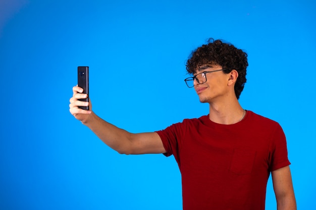 Foto gratuita hombre de camisa roja tomando selfie o haciendo una llamada telefónica y divirtiéndose.