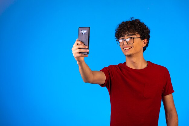 Hombre de camisa roja tomando selfie o haciendo una llamada telefónica.