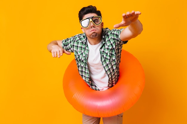 Foto gratuita el hombre con camisa verde, máscara de buceo y círculo inflable representa nadando en el espacio naranja.