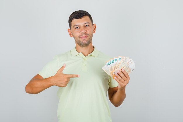 Hombre en camiseta apuntando con el dedo a los billetes en euros y mirando feliz
