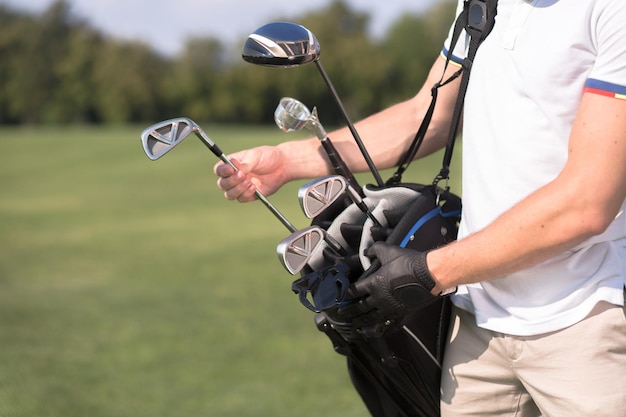 Hombre de camiseta blanca quitando un palo de golf de su bolsa de golf para empezar a jugar