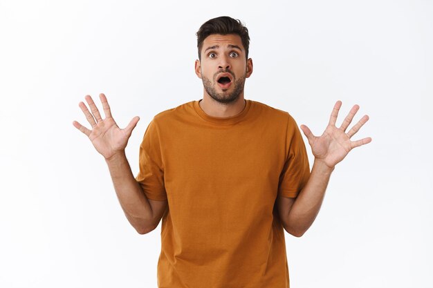 Hombre con camiseta marrón, levantando las manos mientras atrapa algo con expresión de sorpresa inesperada, boca abierta jadeando, levanta las manos hacia los lados