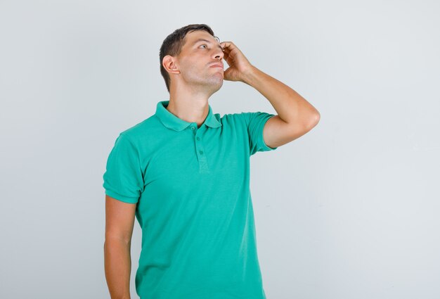 Hombre en camiseta mirando hacia arriba sosteniendo la mano a la cara y mirando pensativo, vista frontal.