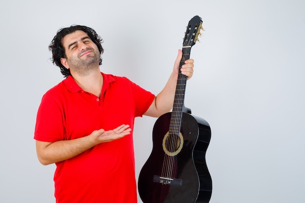 Hombre en camiseta roja mostrando la guitarra y mirando complacido