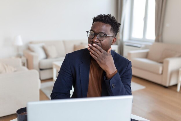 Hombre cansado bostezando después de un largo día de trabajo Temprano en la mañana trabajando El autónomo cansado y soñoliento está bostezando en su casa frente a la pantalla de las computadoras portátiles en el escritorio