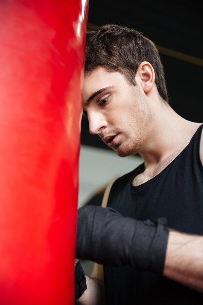 Hombre cansado boxer apoyándose en saco de boxeo