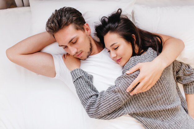 Hombre cansado en camiseta blanca abrazando a esposa mientras duerme