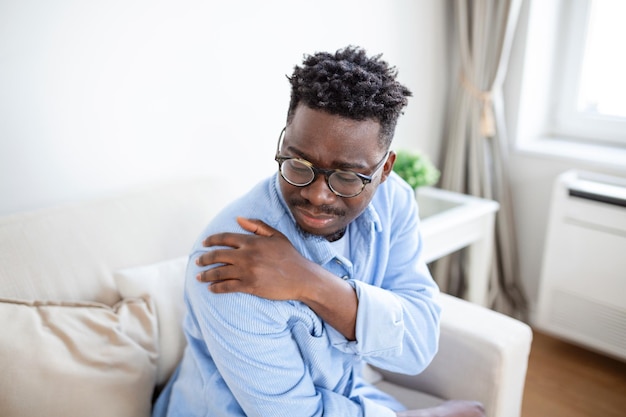 Hombre cansado masajeando el cuello rígido y dolorido músculos tensos fatigados por el trabajo de la computadora en una postura incorrecta mientras se siente herido en la articulación del hombro dolor de espalda dolor concepto de fibromialgia