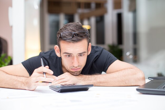 Hombre cansado que miente en el escritorio con la calculadora