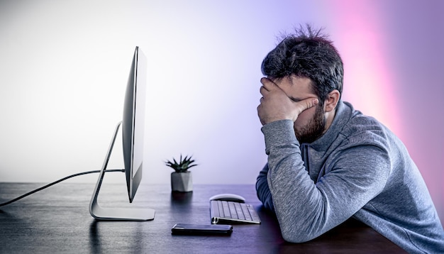 Foto gratuita un hombre cansado se sienta frente a una computadora que cubre su rostro con las manos