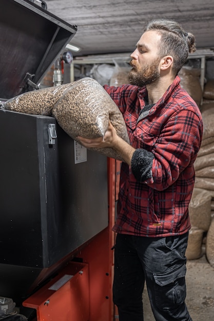 El hombre carga los pellets en la caldera de combustible sólido, trabajando con biocombustibles, calefacción económica.