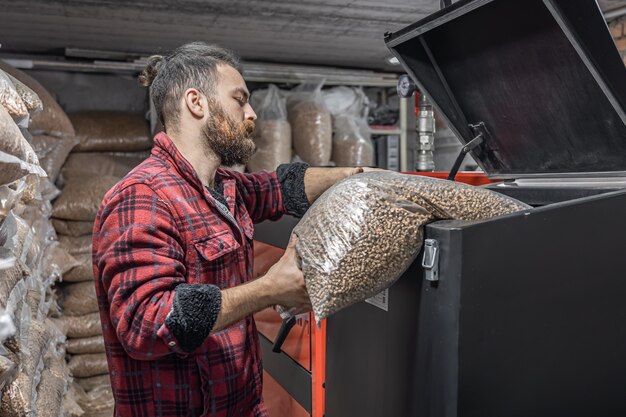 El hombre carga los pellets en la caldera de combustible sólido, trabajando con biocombustibles, calefacción económica.