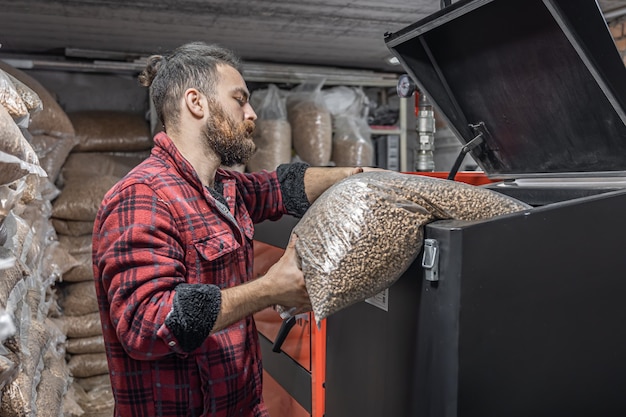 El hombre carga los pellets en la caldera de combustible sólido, trabajando con biocombustibles, calefacción económica.