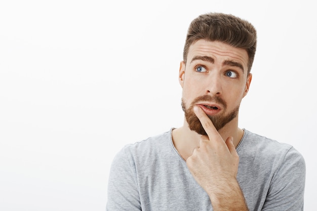 Hombre carismático y reflexivo encantador que intenta pensar en una solución. Novio brunet guapo creativo con barba y ojos azules levantando las cejas mirando la esquina superior izquierda tocando el labio, pensando