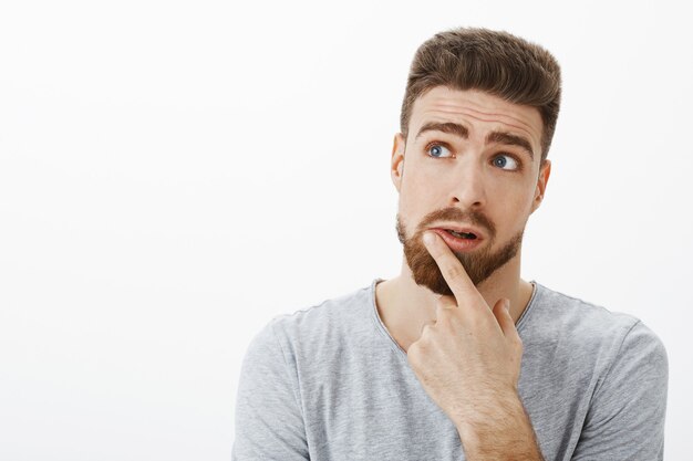 Hombre carismático y reflexivo encantador que intenta pensar en una solución. Novio brunet guapo creativo con barba y ojos azules levantando las cejas mirando la esquina superior izquierda tocando el labio, pensando