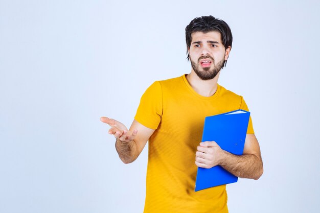 Hombre con una carpeta azul apuntando a su colega del lado izquierdo y hablando con emociones.