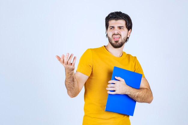 Hombre con una carpeta azul apuntando a su colega del lado izquierdo y hablando con emociones.