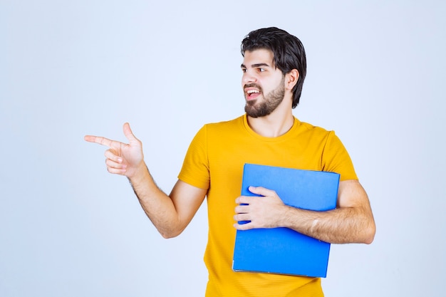 Foto gratuita hombre con una carpeta azul apuntando a su colega del lado izquierdo y hablando con emociones.