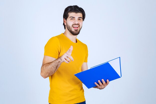 Hombre con carpeta azul apuntando a su colega y sonriendo.