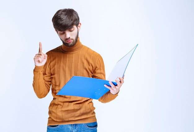 Hombre con una carpeta azul levantando el dedo para llamar la atención.