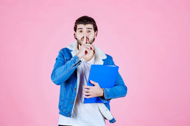 Hombre con una carpeta azul pidiendo silencio