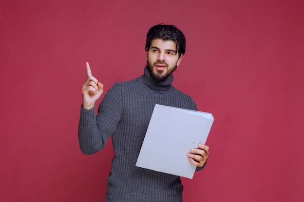 El hombre con la carpeta gris hace que su dedo índice hacia arriba.