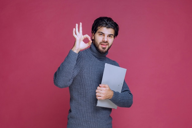 Hombre con carpeta gris hace signo de mano de disfrute.