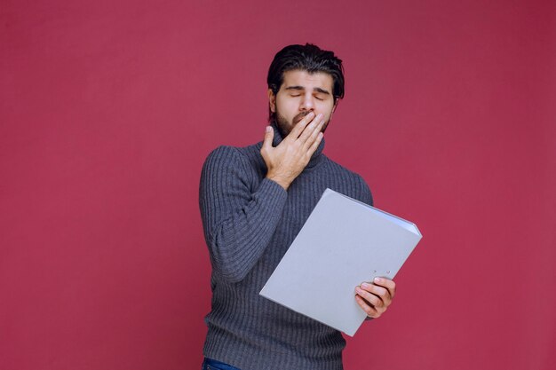 El hombre con carpeta gris parece cansado y con sueño.