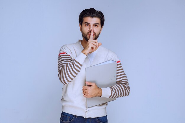 Hombre con carpeta de proyecto pidiendo silencio.