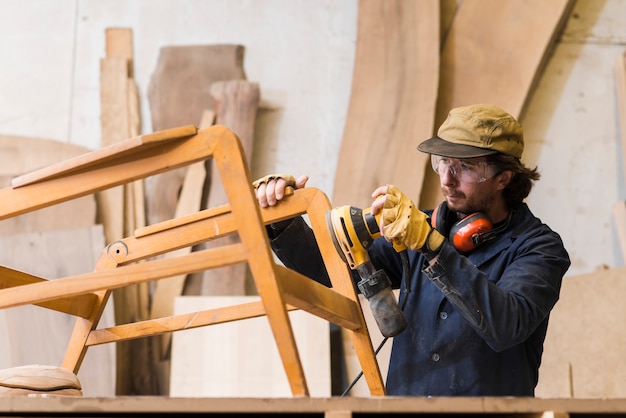 Hombre carpintero lijando una madera con lijadora orbital en un taller