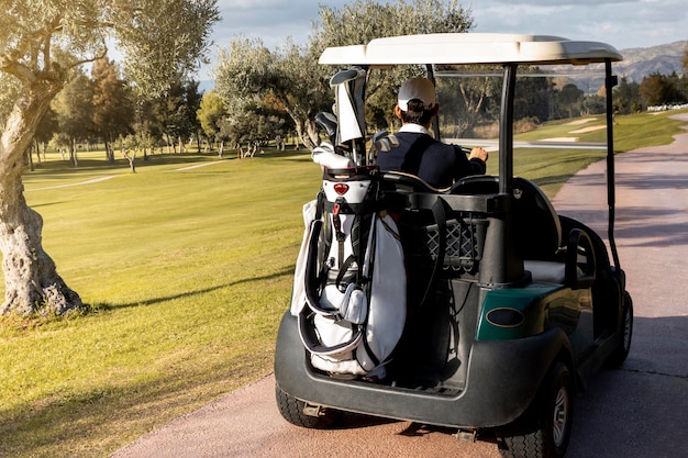 Hombre con carrito de golf llevando palos