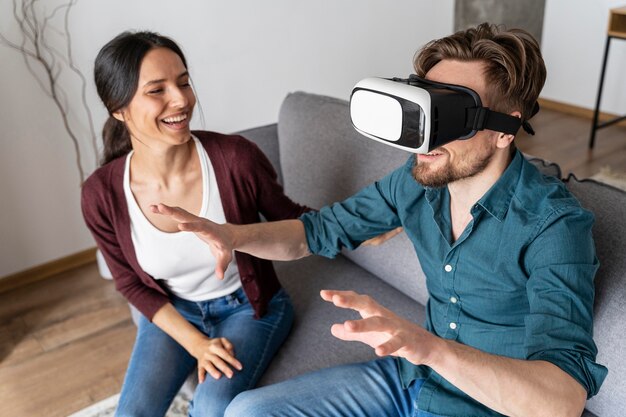 Hombre en casa con casco de realidad virtual junto a la mujer