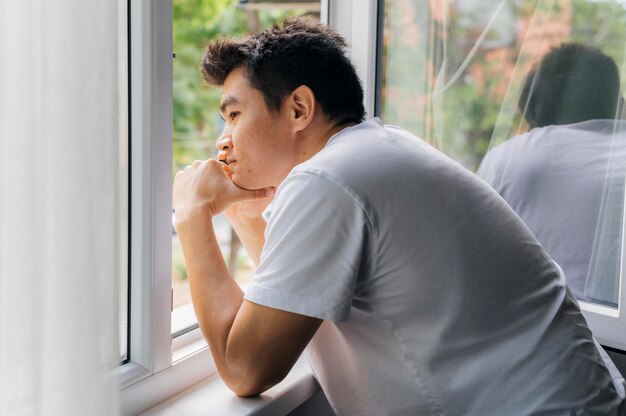 Hombre en casa durante la pandemia mirando por la ventana al aire libre