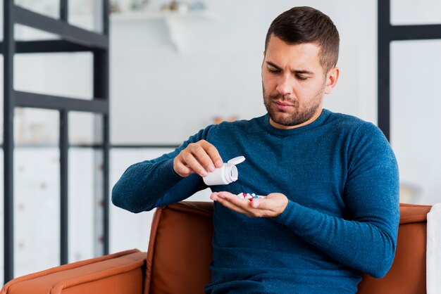 Hombre en casa sentado en el sofá tomando pastillas