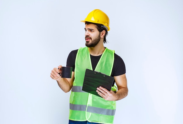 Hombre con casco amarillo con carpeta de proyecto y una taza de café.