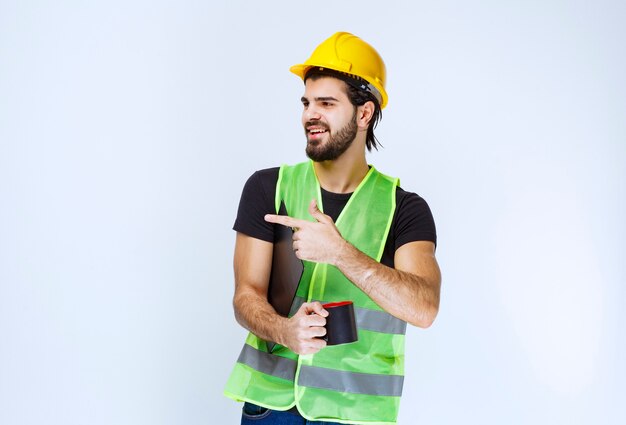 Hombre con casco amarillo con carpeta de proyecto y una taza de café.