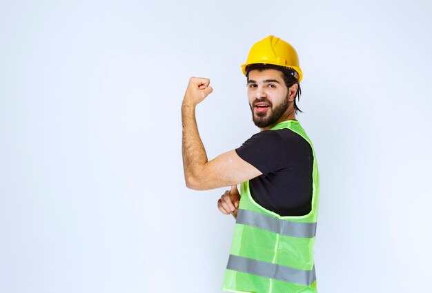 Hombre con casco amarillo mostrando los músculos de su brazo.