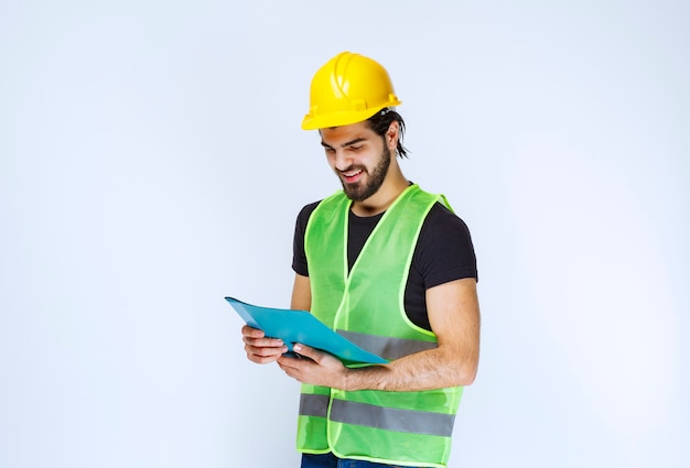 Hombre con casco amarillo sosteniendo y comprobando la carpeta del proyecto azul.