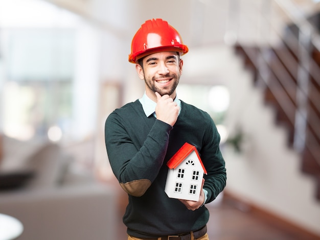 Hombre con casco rojo y una casa pequeña en la mano