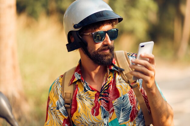 Hombre en casco sentado en moto y usando teléfono móvil