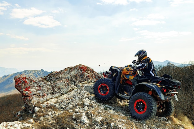 Hombre en casco sentado en quad atv en las montañas