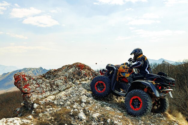 Hombre en casco sentado en quad atv en las montañas