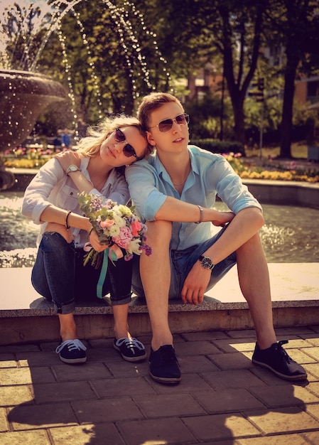 Foto gratuita hombre casual con bicicleta besando a su novia cerca de una fuente en un parque.