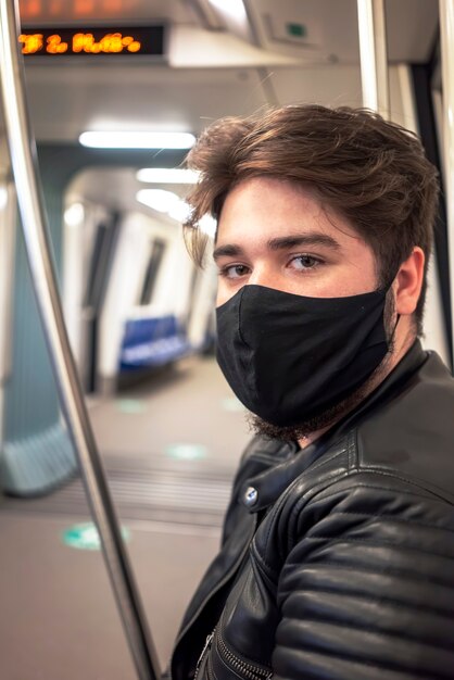 Un hombre caucásico con barba en máscara médica negra, mirando a la cámara en el metro de Bucarest, Rumania