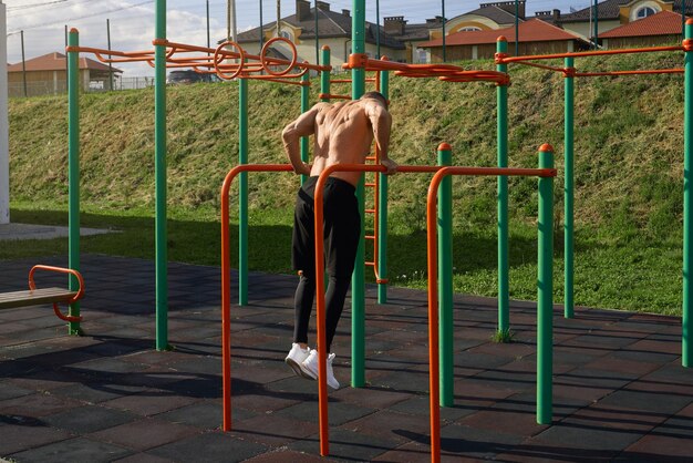 Hombre caucásico sin camisa haciendo ejercicio en barras paralelas al aire libre