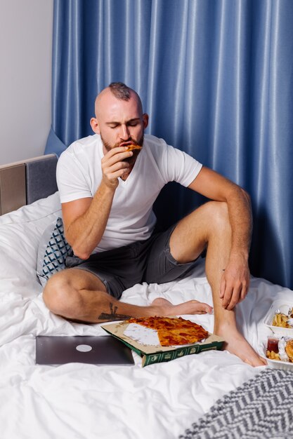 Hombre caucásico con comida rápida en casa en el dormitorio en la cama