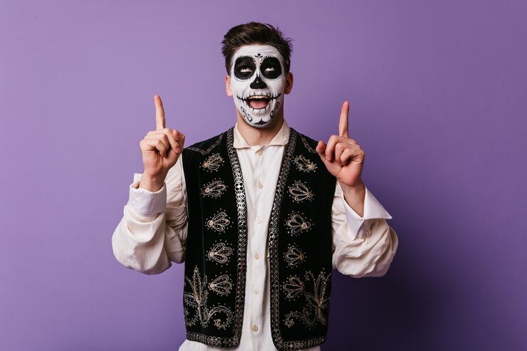 Foto gratuito hombre caucásico complacido en traje mexicano preparándose para la fiesta. modelo masculino entusiasta con maquillaje de halloween divertido posando en la pared púrpura.
