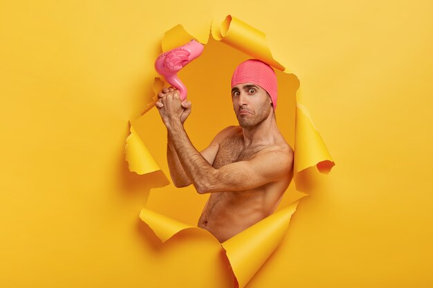 Hombre caucásico desconcertado se prepara para el resort, usa gorro de baño rosa, sostiene un flamenco inflado