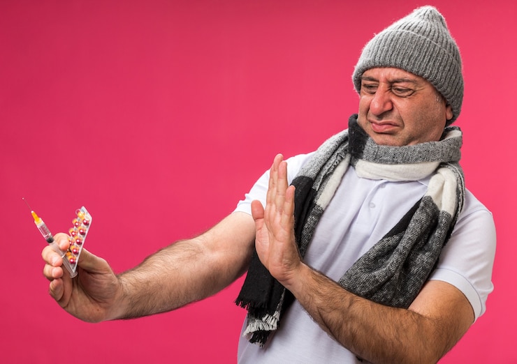 Foto gratuito hombre caucásico enfermo adulto disgustado con bufanda alrededor del cuello con sombrero de invierno sosteniendo y mirando el blister de jeringa y medicamento aislado en la pared rosa con espacio de copia